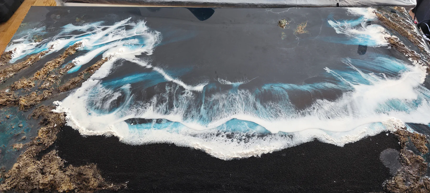 Detalle horizontal de una obra de resina turquesa, blanca, negra y dorada en proceso